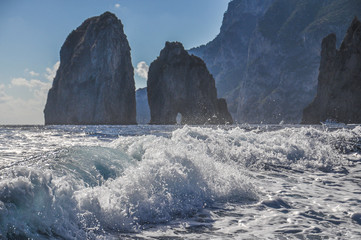 Fototapeta na wymiar The Faraglioni and rocky coast of Capri behind the wake of a boat, Italy