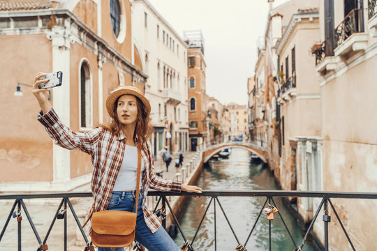 Woman taking selfie photo with smart phone in Venice. Travel female taking self portrait on venetian bridge with beautiful landscape on the background, Venice, Italy.