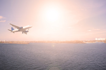 Fototapeta na wymiar Airliner over the river sunset in the city. Landscape, transport, travel.