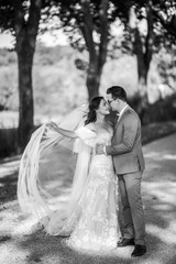Fototapeta na wymiar Beautiful wedding couple. Black and white photo of gorgeous bride in luxury wedding dress with bridal veil and a stylish groom, they hug each other with love