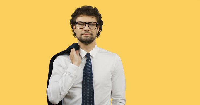 Good looking Caucasian businessman in glasses and tie throwing his jacket over the shoulder on the yellow screen background.
