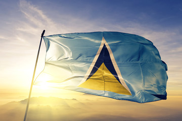 Saint Lucia flag waving on the top sunrise mist fog - obrazy, fototapety, plakaty