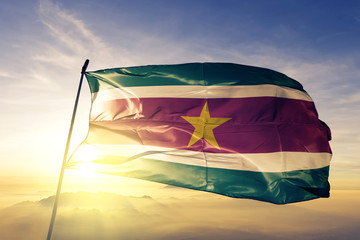 Suriname flag waving on the top sunrise mist fog