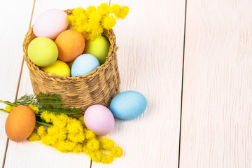 Close up of Colourful Easter Eggs and Mimosa Flowers in a Basket on a Table