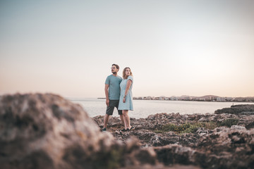 Fototapeta premium Paar spaziert über Felsen am Strand bei Sonnenuntergang