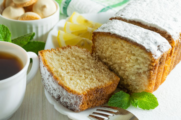 Slices of biscuit cake, a сup of tea and small cookies on a white wooden table.