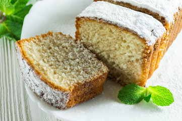 Slices of biscuit cake with powdered sugar, decorated with mint leaves on a white wooden table.