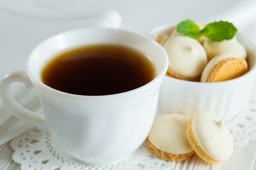 A Cup of tea and small cookies with mint leaves on a white wooden table.