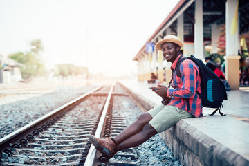 African man traveler playing smartphone waiting for the train on railroad station