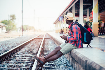 Fototapeta premium African man traveler playing smartphone waiting for the train on railroad station