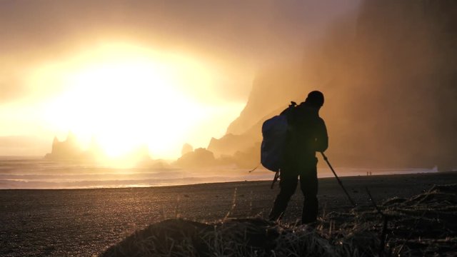 A dramatic scene of a photographer at Vik Black Sand Beach in Iceland seen at Sunset about to set up.