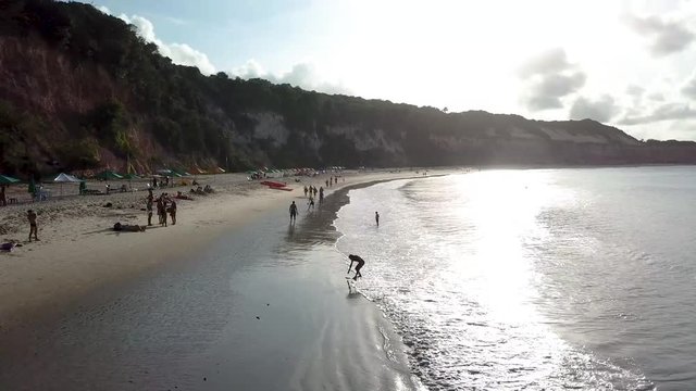 Drone footage. View from above, flying over the beach. People playing on the beach. Sun over the cliff. Coastline of Praia da pipa, Rio grande do norte, brazil.