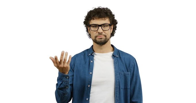 Caucasian man in glasses and jeans shirt doing gesture like so-so with a hand while standing on the white wall screen.