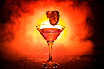 Martini cocktail glass in hand splashing on dark toned smoky background or colorful cocktail in glass with splashes and olives. Party club entertainment. Mixed light. Selective focus