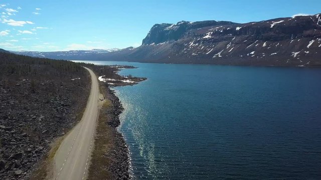 Aerial, drone shot, of a road parallel to tornetrask lake, endless tundra wilderness and snowy, fell mountains, on a sunny, spring day, in Abisko, Kiruna, Lapland, North Sweden