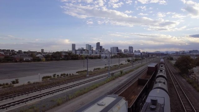 Drone view of downtown Denver, Colorado skyline with trains and train-tracks in the foreground, shot on a cool fall evening with scattered clouds.