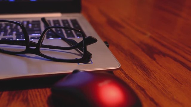 Slider shot moving left to right of glasses resting on top of a laptop computer leaving a wide space on the table beside a mouse