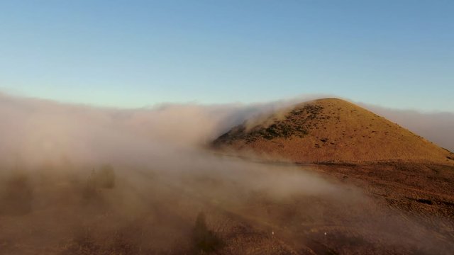 Drone shot of clouds flowing around a volcanic cinder cone on Big Island of Hawaii.