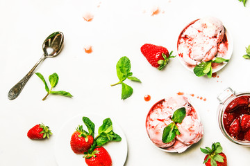 Strawberry ice cream with jam topping, decorated with green mint leaves, gray kitchen table background, top view