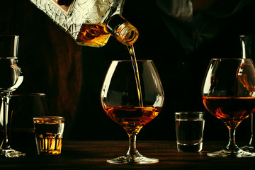 The bartender pours the cognac or brandy in big wine glass on the old bar counter. Vintage wooden background in pub or bar, night mood. Place for text, toning, selective focus