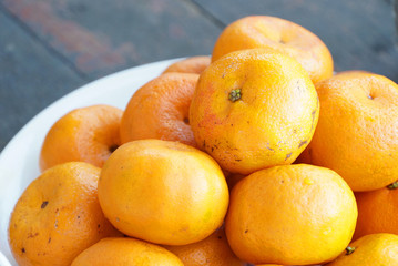 many orange fruits in white plate on wood background