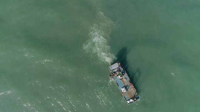 Top down of a crude shellfish working boat or sea vessel. Dark murky waters, water churched up slightly around the boat stern from the propellers