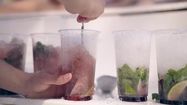 CU, 4k shot: Barman in the summer on the beach prepares refreshing cocktails, with ice, mojito, fruits and berries. Shaking.