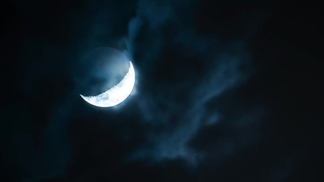 Close or shot of the moving moon crescent behind the clouds