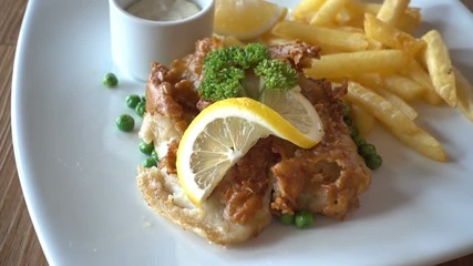 Close up panning shot across fish, chips & peas dinner, supper on white plate, wooden table with slice of lemon garnish.
