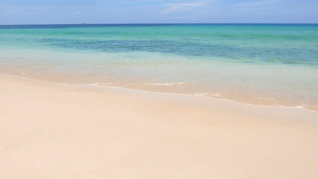 Wide shot of gentle waves on a tropical white sand beach with clear turquoise water.