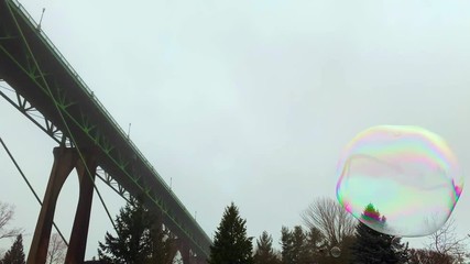 Giant colorful soap bubbles floating around, bridge and cloudy sky in background - Powered by Adobe