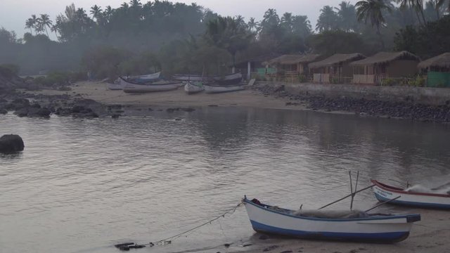 Panning shot across row of grass thatched colourful beach huts on the shoreline of Indian, Goa beach. View of coastal waters in foreground.