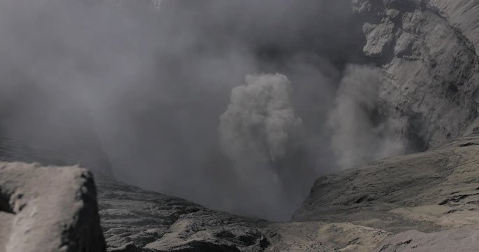 Downward view of Bromo volcanic crater as plumes of smoke, ash clouds emerge through the crater mist.