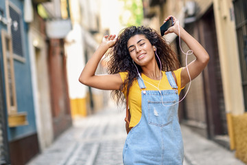 Attractive African girl listening to music with earphones outdoors.
