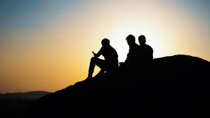 Fototapeta na wymiar Silhouette of group people sits and admiring the sunset on top of mountain.