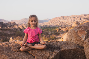 Naklejka na ściany i meble Little cute girl meditating on top of mountain. Portrait of child meditating in lotus pose on the stone