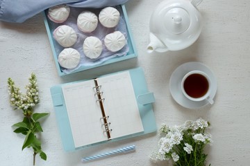 Spring tea.Flat lay.Spring to-do list. marshmallow, blue pen and blue  notebook, cup of tea ,kettle and white flowers on a white background.