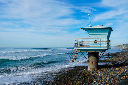 Blue lifeguard tower on a rocky sand beach with clouded blue sky sunny end of day, on Torrey Pines State Beach in California, located in San Diego County.