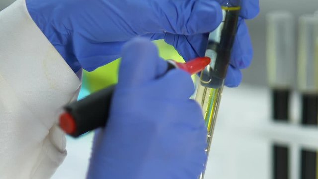 Laboratory worker marking test tube with refined oil sample fuel quality control