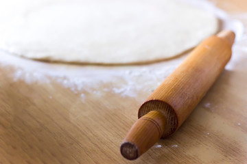Dough for pizza and rolling-pin on wooden table