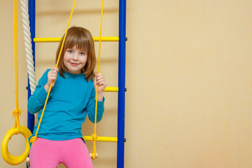 The girl cheerfully sits on a sports ladder.