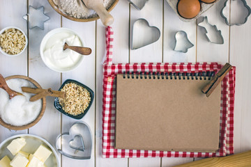 Cooking ingredients and tools near open notebook From above pastry ingredients and cooking tools placed on white wooden table near open notepad with blank pages