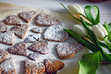 Homemade cookies hearts on a light table near flowers tulips, top view, flat lay. Delicious background for valentine's day or mother's day.