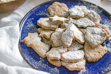 Shortbread homemade cookies of different shapes in a blue plate and adjusted with icing sugar. Next to the ingredients for baking, white wooden background, top view.