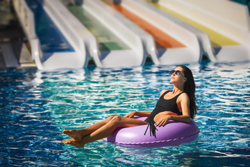 pretty brunette woman in black bikini on the inflatable ring in the swimming pool. Summer Vacation. Enjoying suntan. Weekend on resort