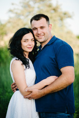 Obraz premium Outdoor shot of young happy couple in love standing on grass in field. Man and woman in sunlight summer park. Happy family in the evening sun light. The concept holiday.