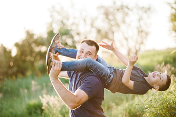 Portrait of happy father carrying on shoulders son on summer vacation. Father's Day. Dad and son playing in the park at the sunset time. Concept of friendly family. Closeup.