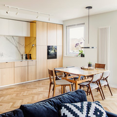 Stylish scandinavian open space with dining and living room interior with design furniture, sofa and family table. Bright and sunny space, marble and red bricks walls, brown wooden parquet. 