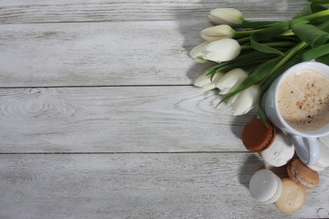 Bunch of white tulips, macaroons and cup of coffee on white wooden table. Good morning concept. Spring menu, cafe, women or mothers day, cappuccino, dessert