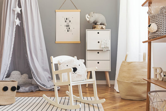 Stylish scandinavian newborn baby room interior with mock up poster , white furnitures, natural toys, hanging grey canopy with stars and teddy bears. Minimalistic and cozy interior with grey walls. 